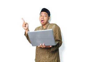 shocked asian muslim man pointing to above with holding laptop isolated on white background photo