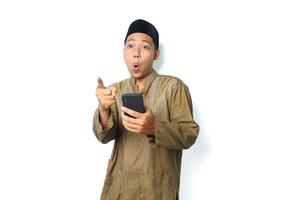 shocked asian muslim man holding mobile phone pointing forward isolated on white background photo