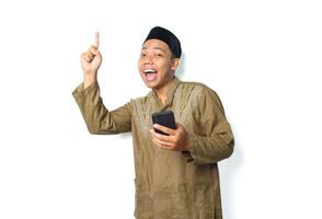 funny asian muslim man screaming while pointing to above with holding moblie phone isolated on white background photo