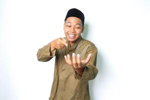 smiling asian muslim man wearing koko clothes pointing to palm with looking at camera isolated on white background photo