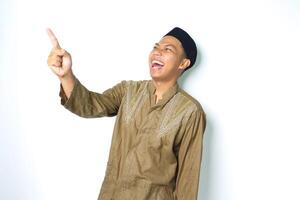 ecstatic asian muslim man wearing islamic dress pointing to empty side with laugh isolated on white background photo