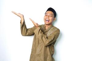 ecstatic asian moslem man wearing islamic dress raising palm to the right side to presenting with laughing expression isolated on whiote background photo