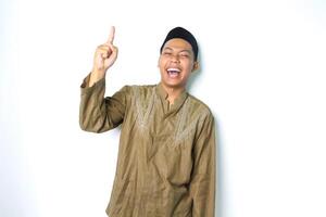 ecstatic asian muslim man wearing islamic dress pointing to above with laugh isolated on white background photo