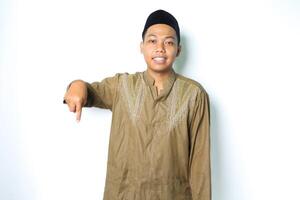 asian muslim man pointing down and smiling at camera wearing islamic dress isolated on white background photo