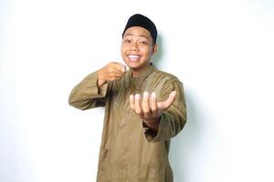 sonriente asiático musulmán hombre vistiendo koko ropa señalando a palma con mirando a cámara aislado en blanco antecedentes foto