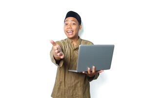 excited asian muslim man holding laptop and reaching hand forward to camera show its you gesture isolated on white background photo