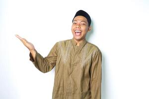 ecstatic asian moslem man wearing islamic dress raising palm to the right side to presenting with laughing expression isolated on whiote background photo