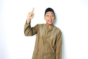 surprised asian muslim man wearing islamic clothes pointing to above isolated in white background photo