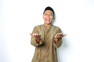 ecstatic asian moslem man wearing islamic dress raising palm at camera to presenting with laughing expression isolated on whiote background photo