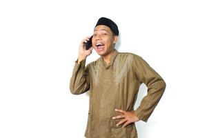 excited asian muslim man have conversation using mobile phone with hand on waist isolated on white background photo