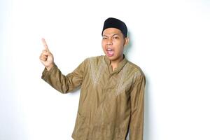 confused asian muslim man pointing to above and looking at camera wearing koko clothes isolated on white background photo