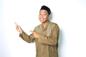 smiling asian muslim man wearing koko clothes pointing to beside with excitement expression looking at camera isolated on white background photo