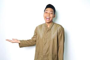 ecstatic asian moslem man wearing islamic dress raising palm to the right side to presenting with laughing expression isolated on whiote background photo