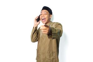 excited asian muslim male pointing at camera while talking using mobile phone isolated on white background photo