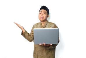 crying asian muslim man presenting to beside with holding laptop isolated on white background photo