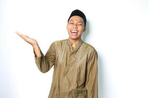extático asiático musulmán hombre vistiendo islámico vestir levantamiento palma a el Derecha lado a presentación con riendo expresión aislado en blanco antecedentes foto