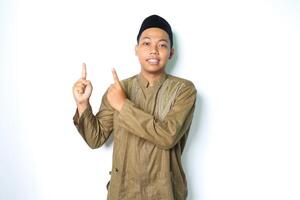 smiling asian muslim man pointing to above wearing islamic dress isolated on white background photo