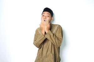 shocked asian muslim man wearing islamic clothes covering his mouth show wow expression isolated on white background photo