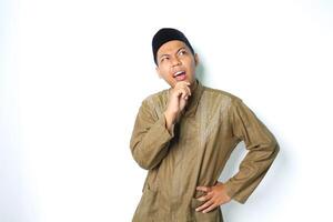 thoughtful asian muslim man thinking seriously with hand on chin wearing koko clothes isolated on white background photo