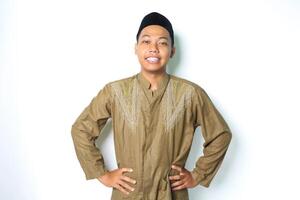 excited asian muslim man wearing islamic dress looking at camera with hands on waist isolated on white background photo