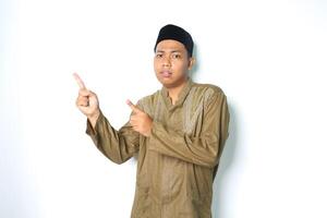 confused asian muslim man pointing to above and looking at camera wearing koko clothes isolated on white background photo