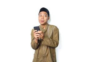 funny asian muslim man holding mobile phone and looking aside thinking idea isolated on white background photo