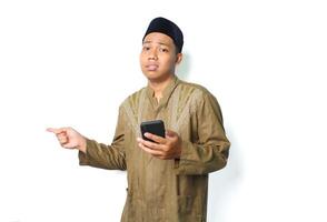 anxious asian muslim man holding mobile phone with pointing to beside show worry expression isolated on white background photo