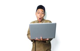 surprised asian muslim man wearing islamic dress holding laptop isolated on white background photo