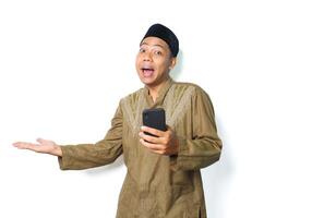 funny asian muslim man presenting copy space with holding mobile phone isolated on white background, looking at camera photo