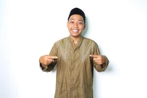 smiling asian muslim man wearing koko clothes pointing to the center with excitement expression looking at camera isolated on white background photo