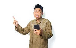 emotional asian muslim man pointing to beside with holding mobile phone isolated on white background photo