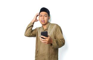 confused asian muslim man holding mobile phone with touching his head isolated on white background photo