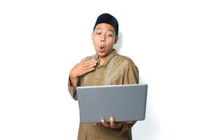 surprised asian muslim man holding laptop with touching his chest isolated on white background photo