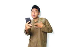 asian muslim man holding mobile phone touching his chest show shocked expression  isolated on white background, looking at camera photo