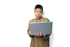 shocked asian muslim man holding laptop looks scared isolated on white background photo