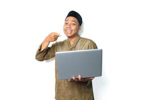 smiling asian muslim man pointing at laptop holding by hand isolated on white background photo