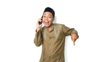 excited asian muslim male pointing down while talking using mobile phone isolated on white background photo