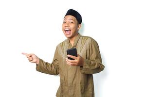 funny asian muslim man screaming while pointing to beside with holding moblie phone isolated on white background photo