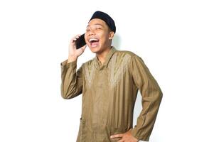 excited asian muslim man speaking using mobile phone with hand on waist isolated on white background, looking at camera photo