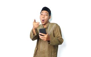 shocked asian muslim man holding mobile phone pointing forward isolated on white background photo