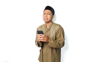 anxious asian muslim man holding mobile phone show worry expression isolated on white background photo