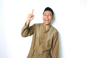 extático asiático musulmán hombre vistiendo islámico vestir señalando a encima con risa aislado en blanco antecedentes foto