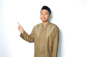 calm asian muslim man smiling at camera wearing koko clothes pointing to beside isolated on white background photo