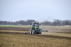 Lush and loosen the soil on the field before sowing. The tractor plows a field with a plow photo