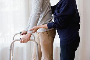 Cropped view of elderly man walking with frame at home, closeup. young male asian using medical equipment to move around his house. Disabled older person in need of professional help photo