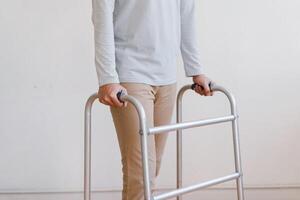 Cropped view of elderly man walking with frame at home, closeup. young male asian using medical equipment to move around his house. Disabled older person in need of professional help photo