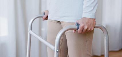 Cropped view of elderly man walking with frame at home, closeup. young male asian using medical equipment to move around his house. Disabled older person in need of professional help photo