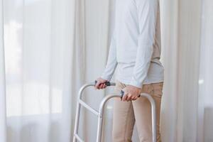 Cropped view of elderly man walking with frame at home, closeup. young male asian using medical equipment to move around his house. Disabled older person in need of professional help photo