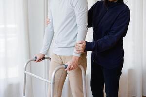 Cropped view of elderly man walking with frame at home, closeup. young male asian using medical equipment to move around his house. Disabled older person in need of professional help photo