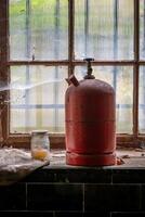 an old red gas bottle on a window photo